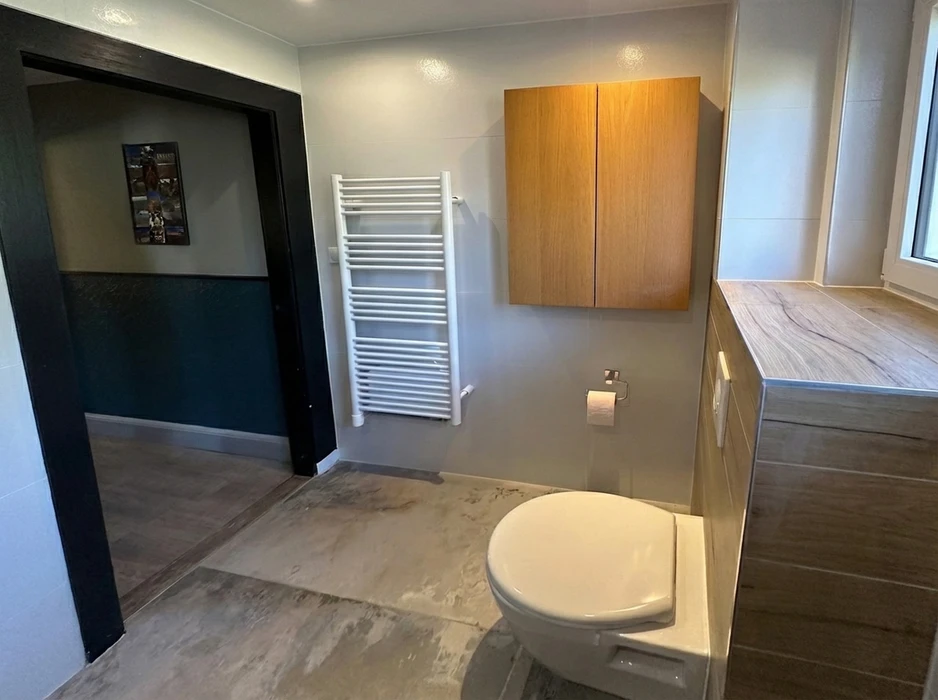 Salle de bains moderne rénovée, WC suspendu blanc, sèche-serviettes à eau blanc, meuble vasque en bois avec plan de travail effet marbre, armoire murale en chêne