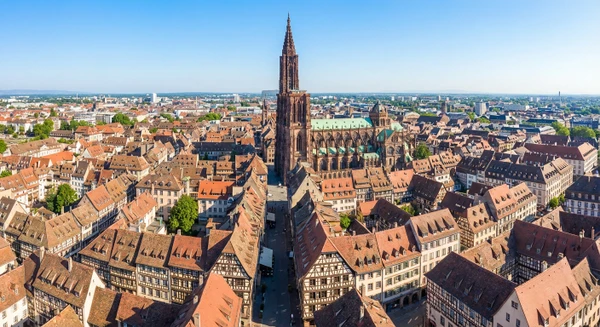 Photographie professionnelle a&eacute;rienne ou perspective &eacute;lev&eacute;e de Strasbourg montrant la cath&eacute;drale et le centre historique avec l'architecture alsacienne typique (maisons &agrave; colombages, toitures de tuiles), entour&eacute; par le tissu urbain et les paysages environnants. L'image doit &ecirc;tre prise par beau temps avec un ciel d&eacute;gag&eacute;, offrant une vue claire et accueillante qui illustre cette ville majeure de la zone d'intervention du chauffagiste ADAO (rayon de 40 km autour de Colmar).