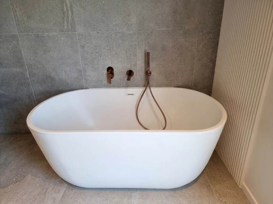 Baignoire îlot autoportante blanche en solid surface, design ovale arrondi, posée sur carrelage grès cérame beige