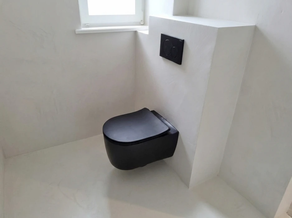 WC suspendu design en céramique noire matte, fixé sur une cloison en béton ciré blanc cassé