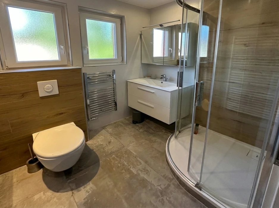 Salle de bain moderne rénovée avec WC suspendu, vasque encastrée sur meuble blanc laqué 2 tiroirs, colonne de douche quart de cercle en verre transparent, sèche-serviettes chromé à eau