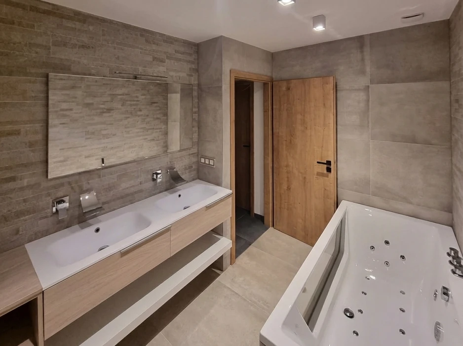 Salle de bain moderne avec double vasque encastrée sur meuble suspendu en bois clair, robinetterie murale chromée, grand miroir rétroéclairé