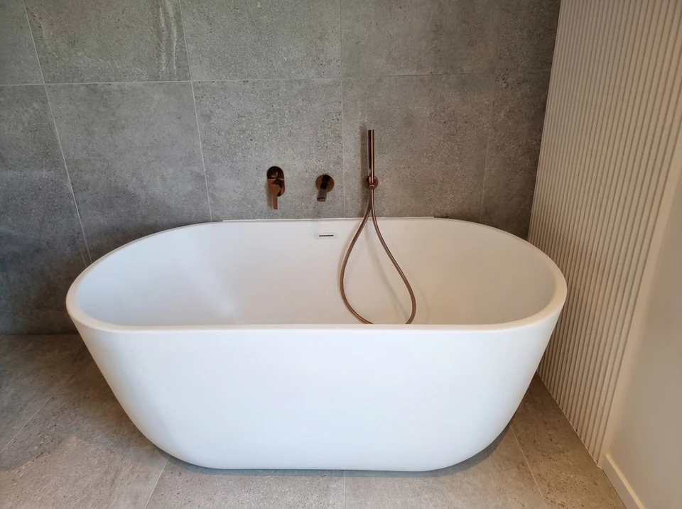 Plombier professionnel à genoux dans une salle de bain moderne, intervenant sous un lavabo blanc avec robinetterie chromée