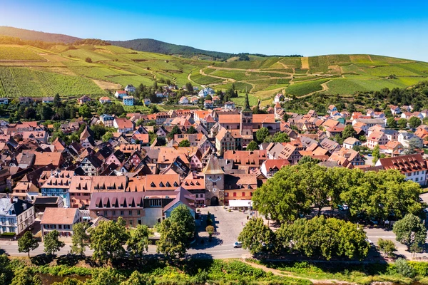 Photographie professionnelle du village de Turckheim en Alsace, montrant une vue du centre-bourg avec l'architecture alsacienne typique (maisons &agrave; colombages, toitures de tuiles color&eacute;es), capt&eacute;e par beau temps avec un ciel d&eacute;gag&eacute;. La perspective doit &ecirc;tre suffisamment large pour montrer l'environnement villageois et les paysages alentour (vignobles, collines), &eacute;voquant clairement la zone g&eacute;ographique de Turckheim dans le Haut-Rhin o&ugrave; intervient le chauffagiste ADAO.